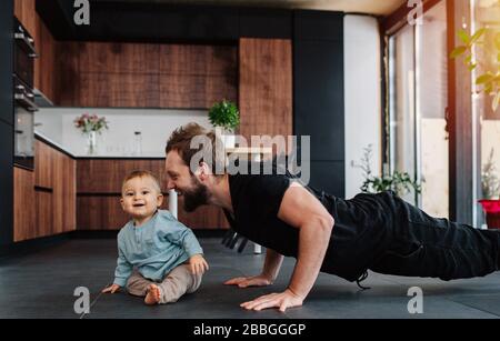 Happy father doing push upps next to his infant baby, moved and amused by him. Stock Photo