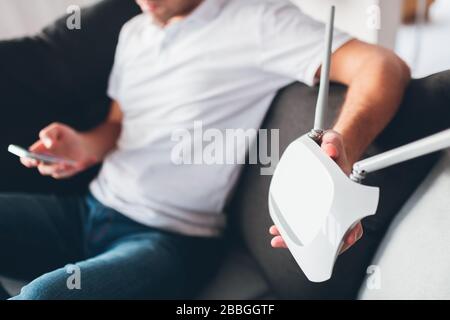 Young man watch tv in his own apartment. Cut view of guy holding wi0fi router in hand and show it on camera. Customizing it. Try to call using Stock Photo