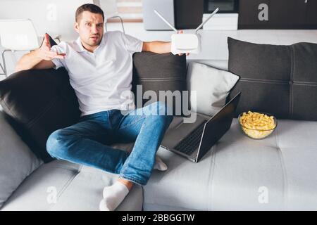 Young man watch tv in his own apartment. Confused distracted guy hold wi-fi router in hand and doesn't know hot to make it work or customize it Stock Photo