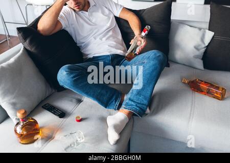 Young man watch tv in his own apartment. Cut view of guy sitting on sofa among opened bottles with whiskey. Suffer from headache or hangover. Problems Stock Photo