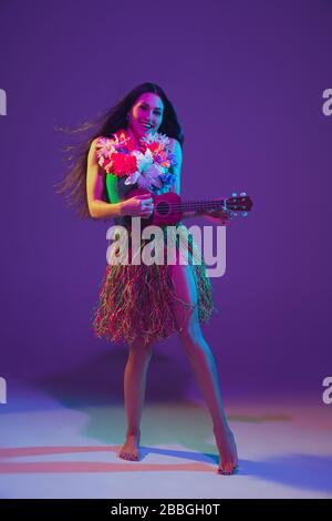 Fabulous Cinco de Mayo female dancer on purple studio background in neon light. Beautiful female model with ukulele, Mexico, Hawaii style. Celebration, holiday, music, beauty and fashion concept. Stock Photo