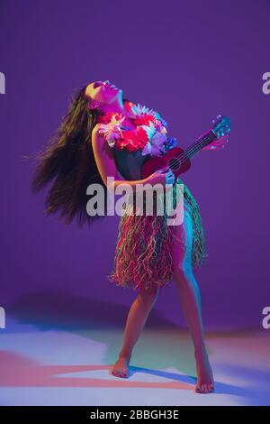 Fabulous Cinco de Mayo female dancer on purple studio background in neon light. Beautiful female model with ukulele, Mexico, Hawaii style. Celebration, holiday, music, beauty and fashion concept. Stock Photo