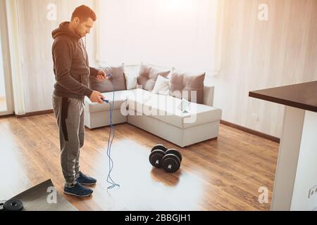 Young ordinary man go in for sport at home. Worksout freshman or amateur hold jump rope in both hands nd ready to use it. Regular ordinary man work on Stock Photo
