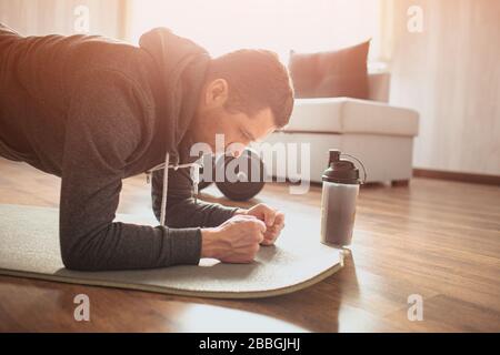 Young ordinary man go in for sport at home. Cut view of amateur sportsman stand in plank position. Freshman working hard on exercise. Concentrated on Stock Photo