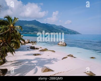 Tropical white beach at Praslin island Seychelles, happy Young couple man and woman during vacation Holiday at the beach relaxing under a palm tree Stock Photo