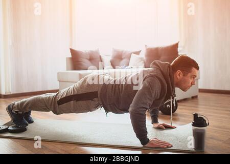 Young ordinary man go in for sport at home. Beginner freshman in exercising guy stand in plank position and look forward. Real picture of patient man Stock Photo