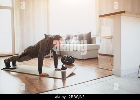 Young ordinary man go in for sport at home. Full size picture of regular ordinary guy stand in plank position alone in room. Beginner try to do his Stock Photo
