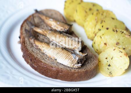 Canned sprats on rye bread served with herb baked potatoes Stock Photo