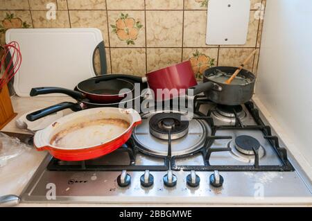 A dirty kitchen with used and unclean pots and pans on a greasy cooker or stove covered in spilt food. Stock Photo