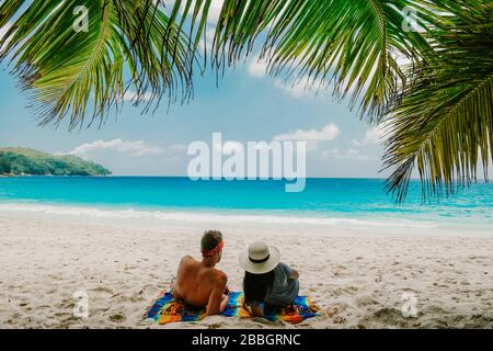 Tropical white beach at Praslin island Seychelles, happy Young couple man and woman during vacation Holiday at the beach relaxing under a palm tree Stock Photo