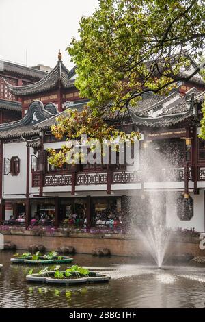 Shanghai, China - May 4, 2010: Yu garden off Yuyuan shopping streets. Pond with green foliage above, fountain and traditional Chinese architecture oin Stock Photo