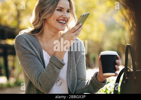 Woman sitting outdoors talking on phone. Female with coffee having a phone call outside in the city. Stock Photo