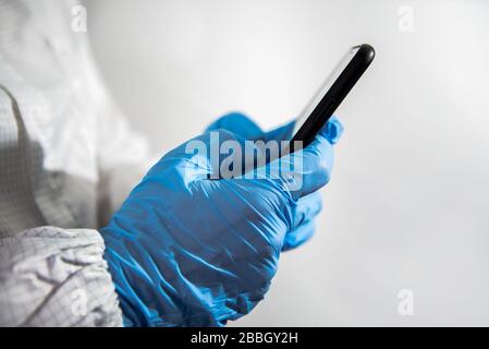 Scientist using smartphone in the scientific chemical laboratory. Doctor hands with blue gloves using phone device. Coronavirus has caused emergency s Stock Photo