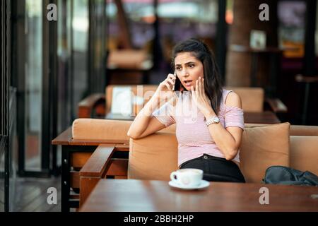 Young woman speak with phone and have a suprised and worried face in an elegance cafe Stock Photo