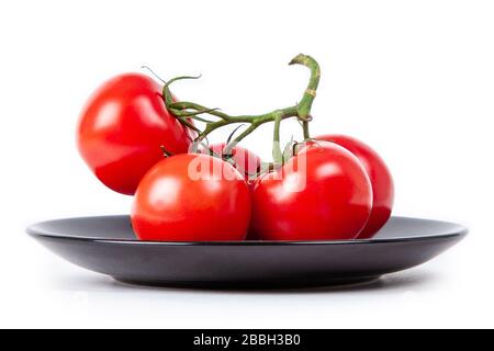 five tomatoes on a branch on a black plate isolated on white background Stock Photo