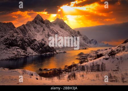 shafts of sunlight shining through clouds over the snowcapped mountains around the fjord. Stock Photo