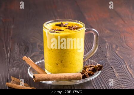 Ayurvedic golden turmeric latte milk made with turmeric and other spices, on wooden background. Healthy medicine drink. Stock Photo