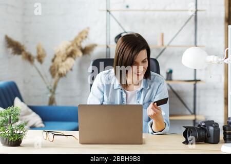 Young freelancer in home office holding credit card and using laptop. Online shopping, online payments. Booking tickets online. Modern technologies Stock Photo