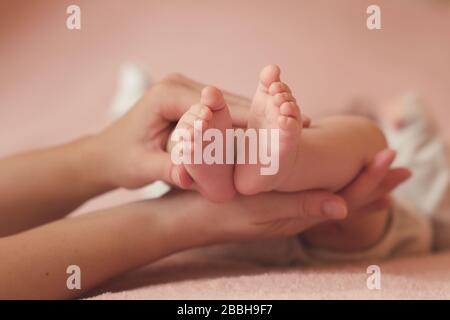 Mother holding baby feet in bed over pink background close up. Motherhood. Maternity.