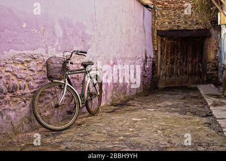 Old bicycle and walls in a village. The walls are purple and there is a wooden door Stock Photo