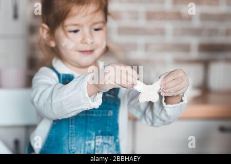 Smiling child girl 3-4 year old making homemade cookies with dough in kitchen close up. Childhood. Stock Photo
