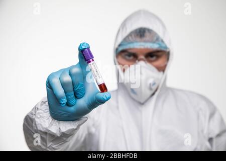 Medic man wearing HAZMAT protective clothing holding test tube filled with blood against gray background. Stock Photo