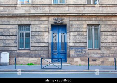High blue wooden door with two narrow windows on the grey building facade, Bordeaux, France Stock Photo