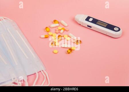 Medical disposable masks, pills and electronic thermometer on a pink background. Protection against influenza virus and pneumonia. Healthcare and medical concept. Stock Photo