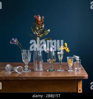 Dried flowers in glass glasses on a wooden table opposite a dark blue wall. Art card. Design. Copy space. Stock Photo