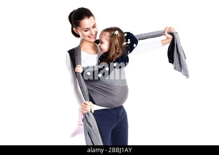 Mother tightening a woven baby wrap carrier with toddler girl in Stock Photo