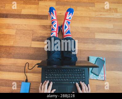 Man wearing union jack flag sock sitting on wooden floor with laptop. Working from home, self isolation, social distancing, Coronavirus... concept Stock Photo