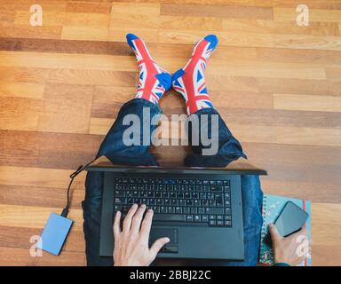 Man wearing union jack flag sock sitting on wooden floor with laptop. Working from home, self isolation, social distancing, Coronavirus... concept Stock Photo