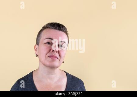 Very short-haired caucasian adult woman in dark sweater looking at us with light smile. Real face without make-up. Copy space. Stock Photo