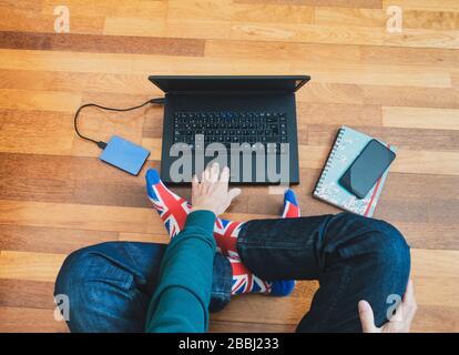 Man wearing union jack flag sock sitting on wooden floor with laptop. Working from home, self isolation, social distancing, Coronavirus... concept Stock Photo