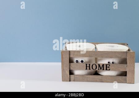 Two rolls of toilet paper with artificial eyes in a wooden box with the inscription Home on the grey blue background Stock Photo
