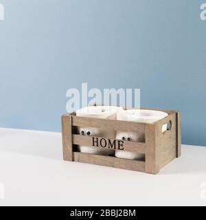 Two rolls of toilet paper with artificial eyes in a wooden box with the inscription Home on the grey blue background Stock Photo