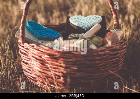 Basket with food and accessories for a romantic lovers picnic on the grass in sunset light. Stock Photo