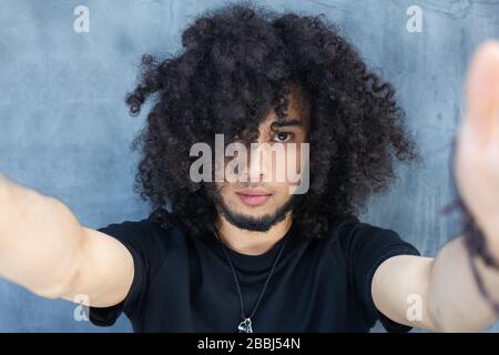 Handsome young African man making selfie while standing against grey background. Afro hair. Stock Photo