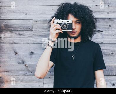 African american man with typical afro hair takes a picture of a vintage camera against a background of old boards Stock Photo