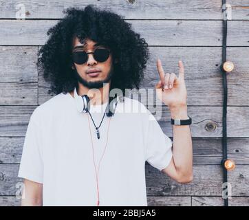 Portrait of a smiling african american young man, shows the gesture of the horns on old wooden background. Afro hairstyle and beard. Stock Photo