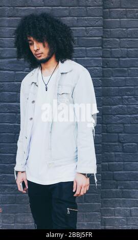 Young black man with afro hair posing on graphite background. Outside. Dressed in a jeans jacket, black trousers. Fashion. Street style. Stock Photo