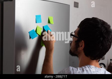 Hispanic young man taking and reading sticky posticks in his fridge Stock Photo