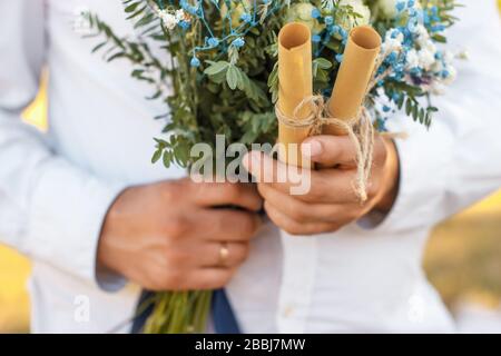Close up view on two rolled paper sheets with wedding vowes in groom hand. Stock Photo