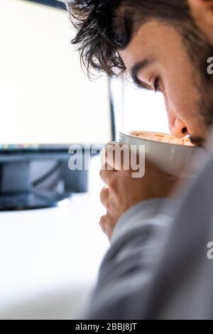Person drinking coffee from a cup in front of the computer on a desk. Stock Photo