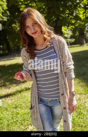 Lovely young woman walking in the park and holding a red apple Stock Photo