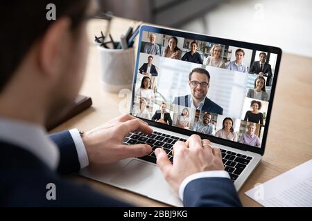 Rear view of businessman speak on web conference with diverse colleagues using laptop Webcam, male employee talk on video call with multiracial cowork Stock Photo
