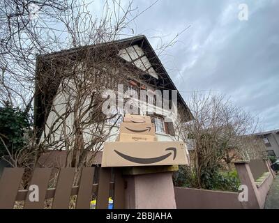 Strasbourg, France - Feb 26, 2020: Low angle view of multiple stacks of Amazon Prime cardboard parcels on the stone fence of modern typical Alsatian house in background Stock Photo