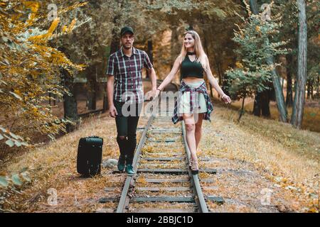 A young couple of lovers missed the train. Walking on the rails in the autumn forest waiting for the next train. Stock Photo