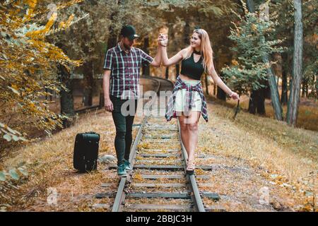 A young couple of lovers missed the train. Walking on the rails in the autumn forest waiting for the next train. Stock Photo