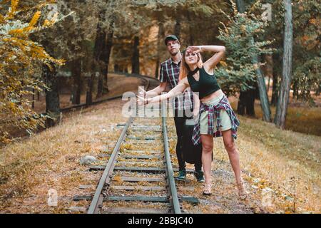 A young couple of lovers missed the train. Hitchhikers on the rails in the autumn forest waiting for the next train. Stock Photo